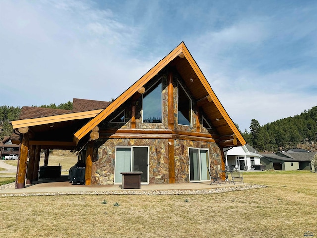 back of house with stone siding, a shingled roof, a lawn, and a patio