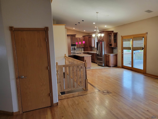 kitchen featuring hanging light fixtures, backsplash, light wood-type flooring, stainless steel appliances, and a center island