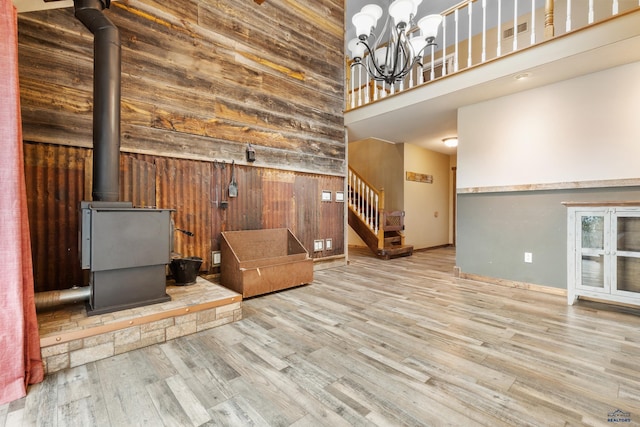 unfurnished living room featuring a chandelier, a high ceiling, wooden walls, and light hardwood / wood-style floors