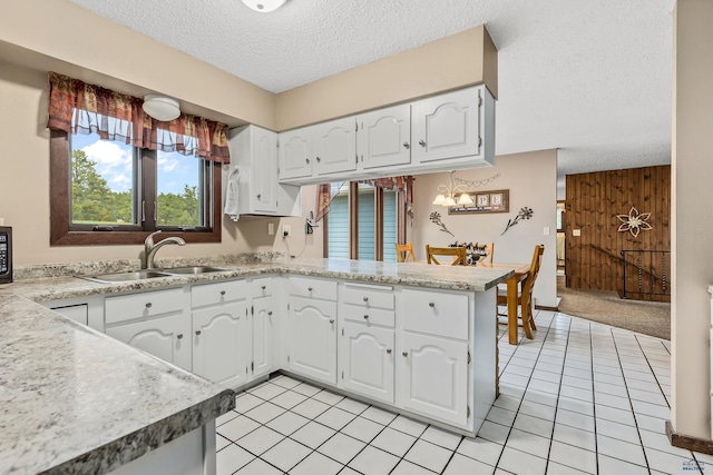 kitchen with white cabinetry, wooden walls, sink, and kitchen peninsula