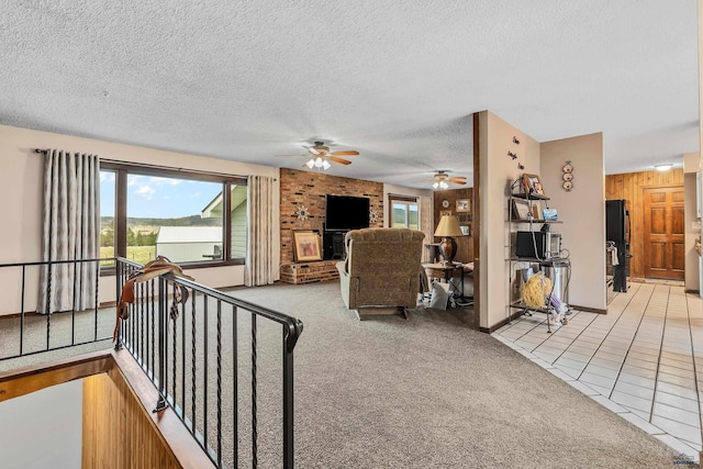 living room featuring light carpet, ceiling fan, a textured ceiling, a fireplace, and wooden walls