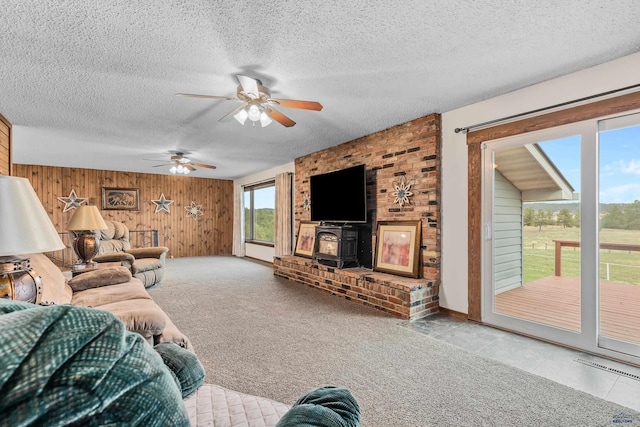 living room with ceiling fan, a wood stove, a textured ceiling, and wooden walls