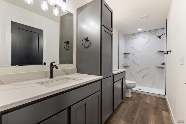 bathroom featuring wood-type flooring, vanity, toilet, and tiled shower