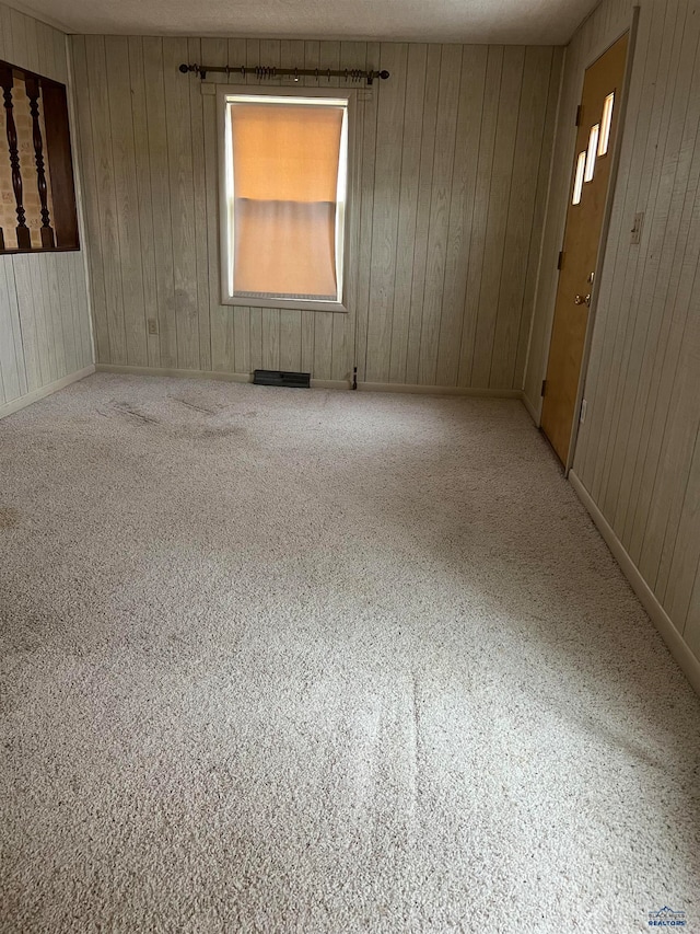 carpeted empty room featuring wooden walls