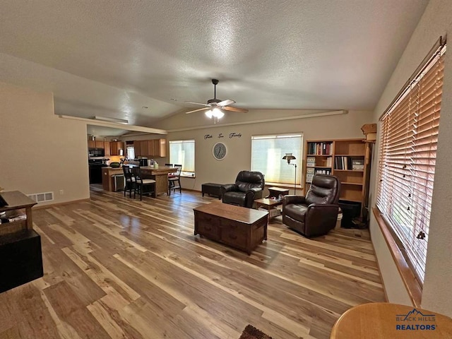 living room with ceiling fan, wood-type flooring, plenty of natural light, and lofted ceiling