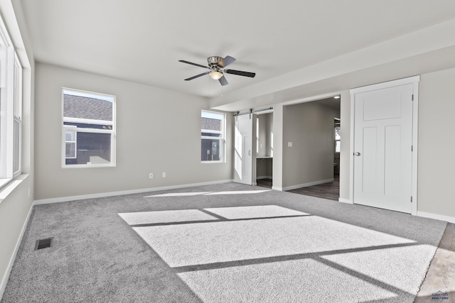 unfurnished bedroom with a barn door, carpet flooring, baseboards, and a ceiling fan