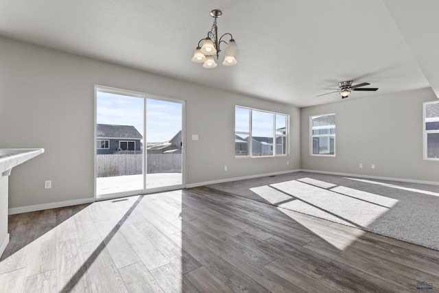 unfurnished living room with ceiling fan with notable chandelier, dark wood-style flooring, and baseboards