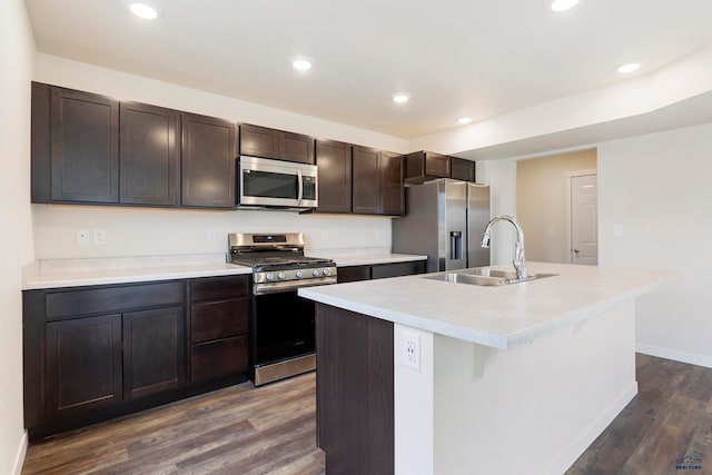 kitchen with dark brown cabinetry, an island with sink, appliances with stainless steel finishes, dark wood-type flooring, and light countertops