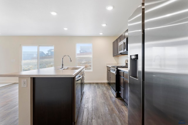 kitchen with a kitchen island with sink, stainless steel appliances, dark wood-style flooring, a sink, and light countertops