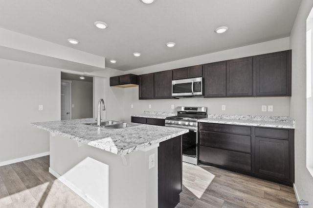 kitchen with appliances with stainless steel finishes, a sink, an island with sink, light wood-type flooring, and recessed lighting