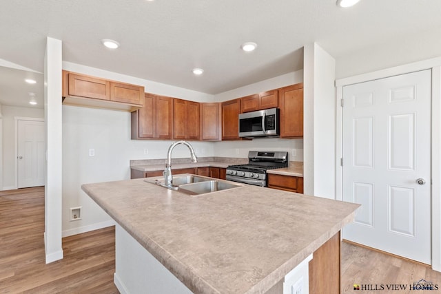 kitchen with light hardwood / wood-style floors, stainless steel appliances, sink, and an island with sink