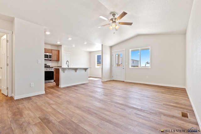 unfurnished living room with vaulted ceiling, a textured ceiling, sink, ceiling fan, and light hardwood / wood-style flooring