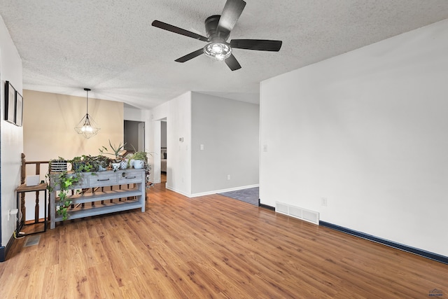 empty room with hardwood / wood-style flooring, ceiling fan with notable chandelier, and a textured ceiling