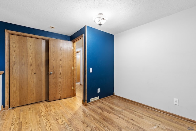 unfurnished bedroom with light wood-type flooring, a textured ceiling, and a closet