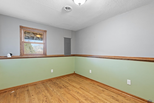 spare room with a textured ceiling, light wood-type flooring, and electric panel