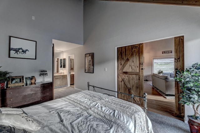 bedroom featuring a barn door, ensuite bathroom, high vaulted ceiling, and light colored carpet