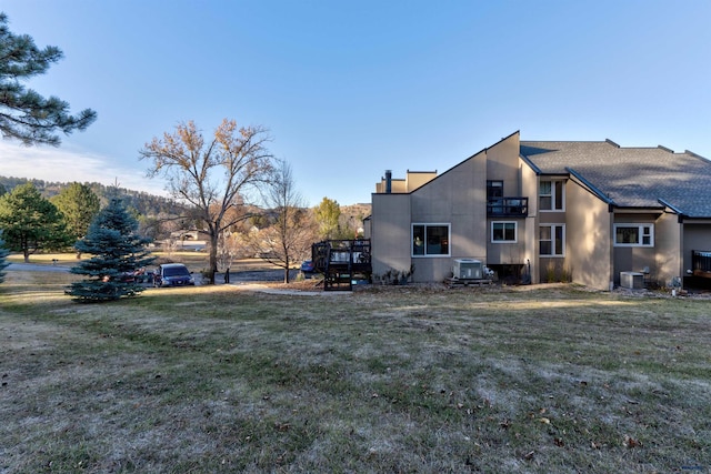 view of side of property with a lawn, central AC unit, and a balcony