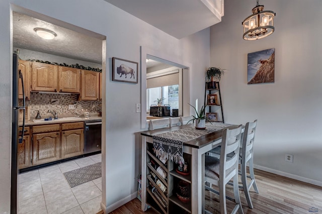 kitchen with sink, stainless steel dishwasher, backsplash, light hardwood / wood-style floors, and decorative light fixtures