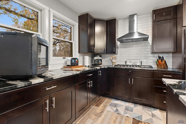 kitchen featuring wall chimney exhaust hood, stainless steel gas cooktop, tasteful backsplash, light hardwood / wood-style floors, and dark brown cabinets