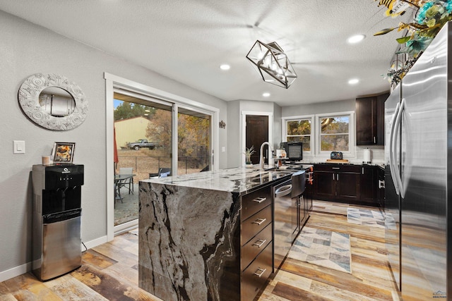 kitchen featuring stainless steel appliances, light hardwood / wood-style floors, a healthy amount of sunlight, and an island with sink