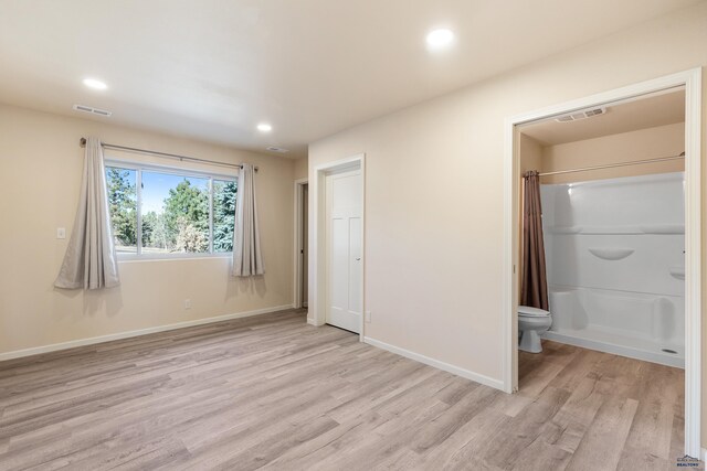 unfurnished bedroom featuring ensuite bath and light hardwood / wood-style floors