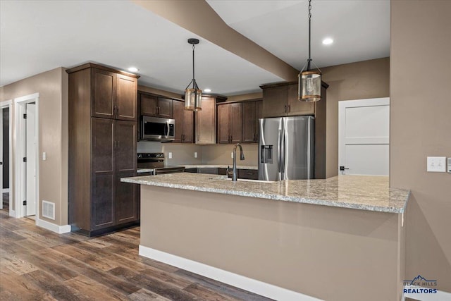 kitchen featuring light stone countertops, appliances with stainless steel finishes, dark hardwood / wood-style flooring, dark brown cabinetry, and pendant lighting