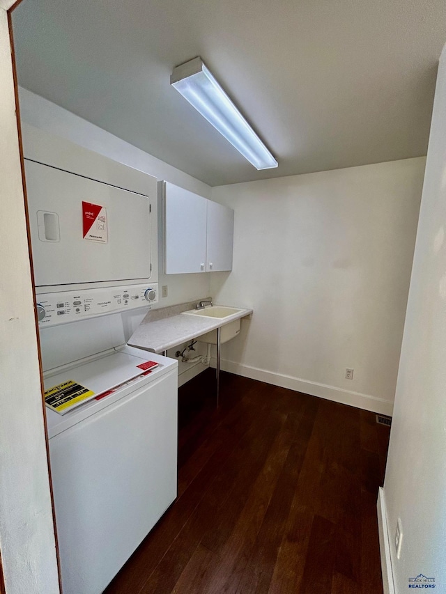 laundry area featuring sink, dark hardwood / wood-style floors, cabinets, and stacked washer / dryer