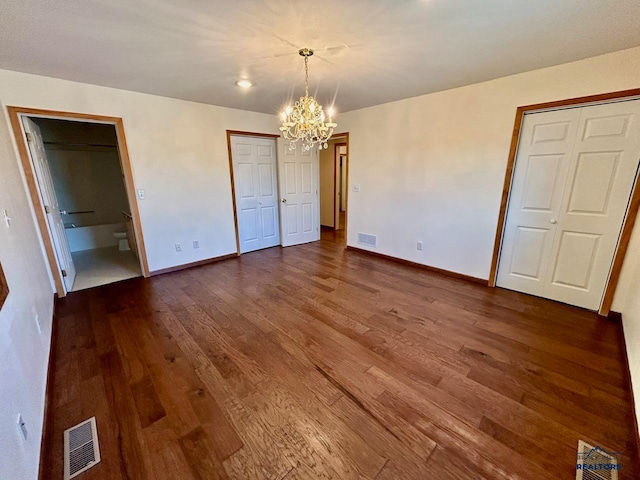 unfurnished bedroom featuring connected bathroom, dark hardwood / wood-style floors, and an inviting chandelier