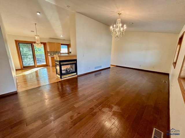 unfurnished living room featuring hardwood / wood-style flooring, a multi sided fireplace, lofted ceiling, and an inviting chandelier