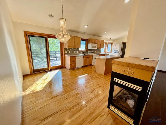 kitchen with tasteful backsplash, light hardwood / wood-style floors, decorative light fixtures, white appliances, and a kitchen island