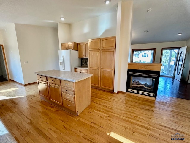 kitchen featuring white refrigerator with ice dispenser, a multi sided fireplace, light hardwood / wood-style flooring, a kitchen island, and stainless steel refrigerator