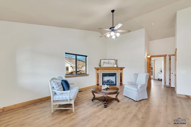 living area with ceiling fan, a fireplace, high vaulted ceiling, and light hardwood / wood-style flooring