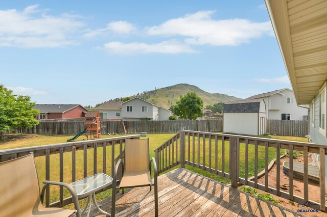 wooden terrace with a mountain view, a playground, a storage unit, and a lawn