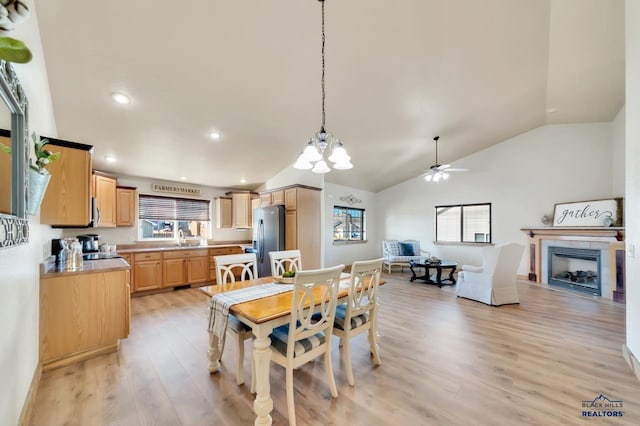 dining space with ceiling fan with notable chandelier, sink, a tile fireplace, light hardwood / wood-style flooring, and lofted ceiling