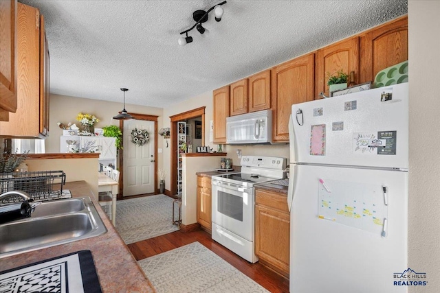 kitchen featuring a textured ceiling, white appliances, sink, decorative light fixtures, and dark hardwood / wood-style floors