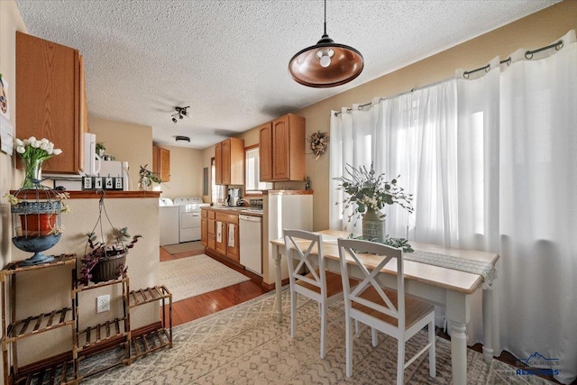 kitchen featuring white dishwasher, a textured ceiling, decorative light fixtures, light hardwood / wood-style floors, and washing machine and clothes dryer