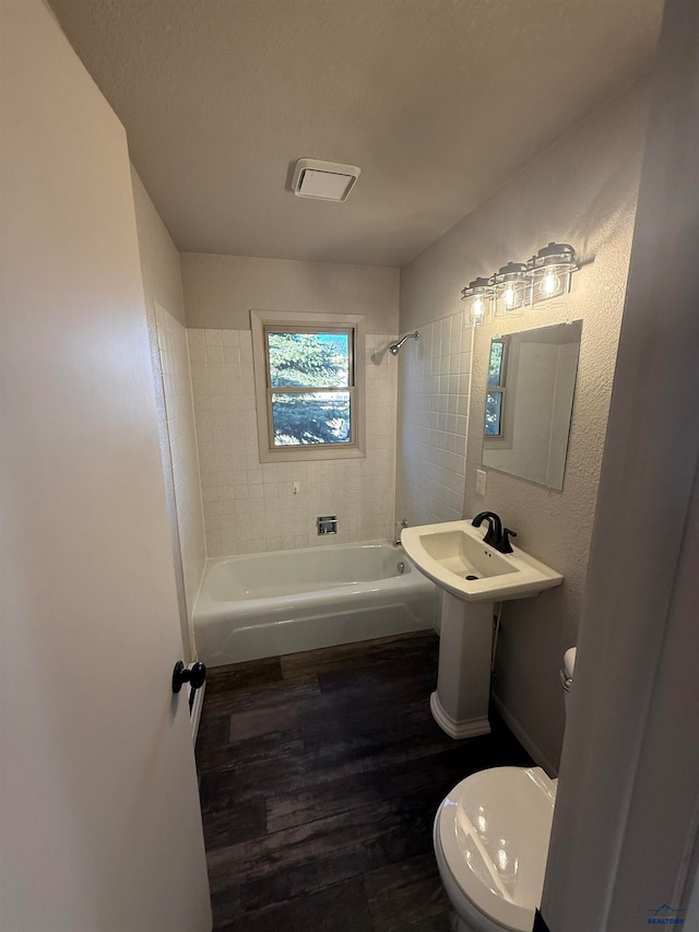 bathroom with hardwood / wood-style flooring, tiled shower / bath combo, toilet, and a textured ceiling