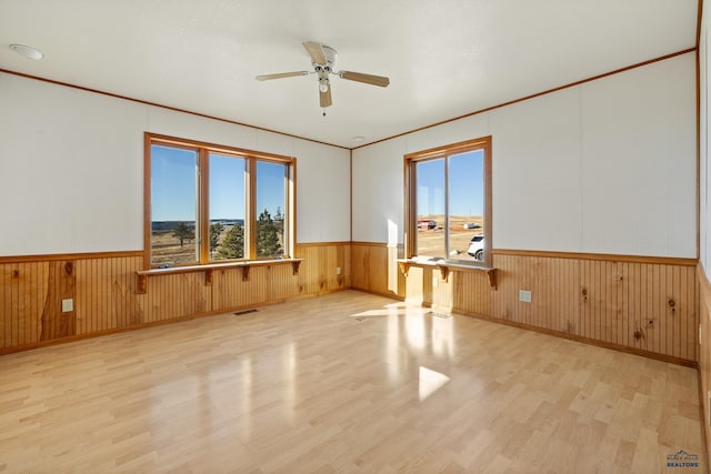 unfurnished room featuring light hardwood / wood-style flooring, ceiling fan, and wooden walls