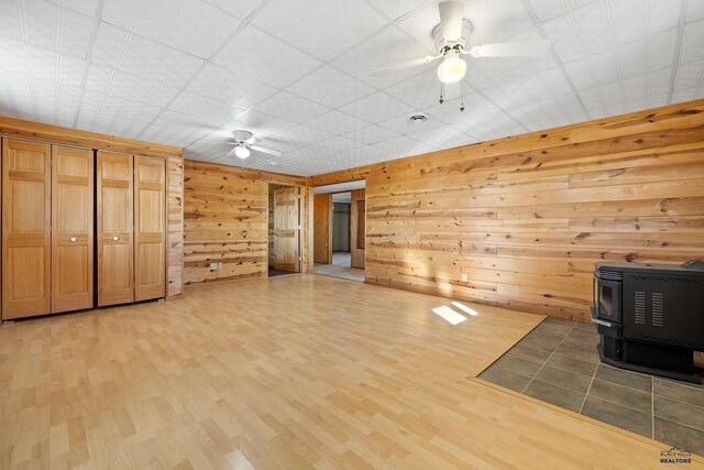 unfurnished living room featuring heating unit, ceiling fan, hardwood / wood-style floors, a wood stove, and wood walls