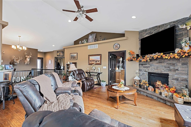 living room with wood-type flooring, ceiling fan with notable chandelier, vaulted ceiling, and a stone fireplace