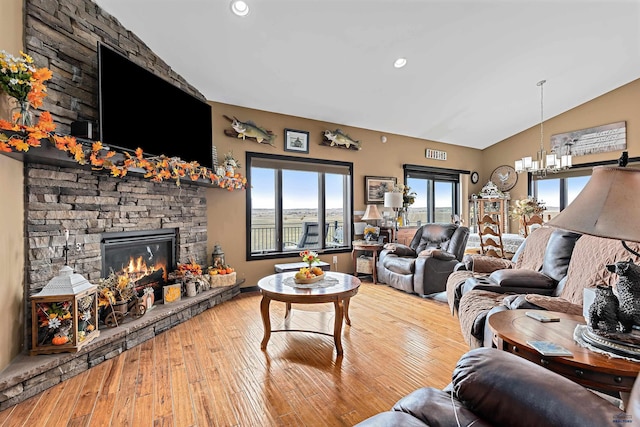 living room with light hardwood / wood-style floors, vaulted ceiling, and a stone fireplace