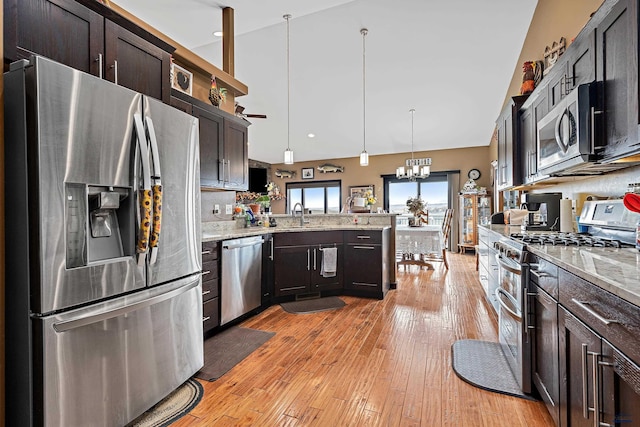 kitchen featuring dark brown cabinetry, light stone countertops, hanging light fixtures, appliances with stainless steel finishes, and light wood-type flooring