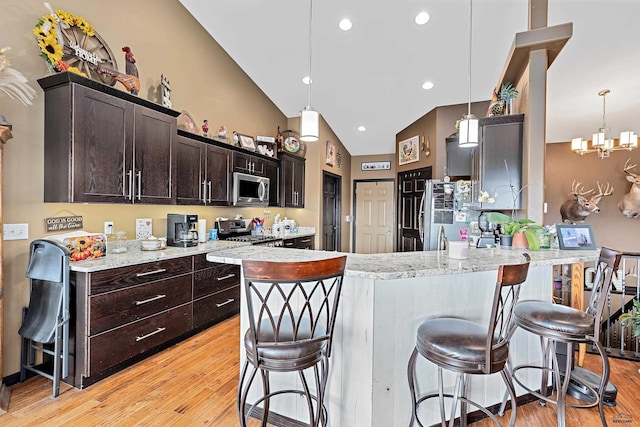 kitchen with a breakfast bar, hanging light fixtures, stainless steel appliances, and light wood-type flooring