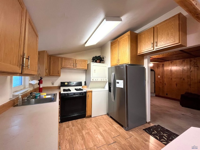 kitchen with light wood-type flooring, gas stove, sink, stainless steel fridge with ice dispenser, and stacked washer and dryer