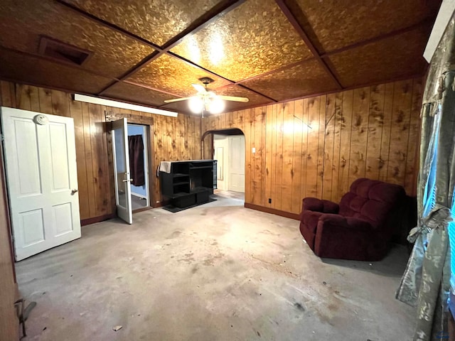 basement with a wood stove, wooden walls, and ceiling fan