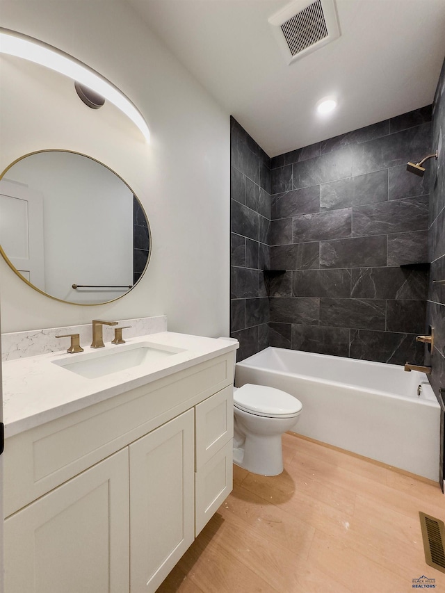 full bathroom featuring vanity, hardwood / wood-style floors, tiled shower / bath combo, and toilet