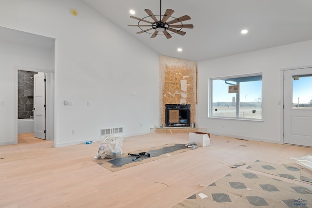 unfurnished living room featuring a stone fireplace, a wealth of natural light, light hardwood / wood-style flooring, and ceiling fan