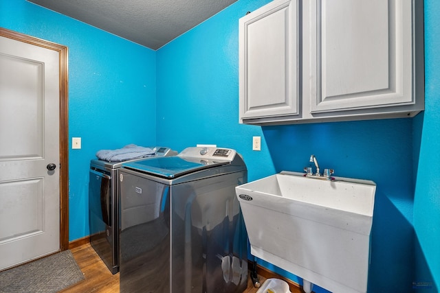 laundry room with cabinets, a textured ceiling, sink, separate washer and dryer, and hardwood / wood-style floors