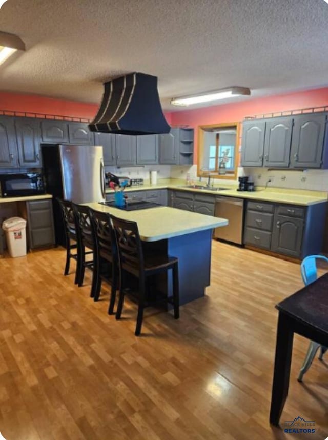 kitchen featuring a breakfast bar, a textured ceiling, stainless steel appliances, and light hardwood / wood-style floors