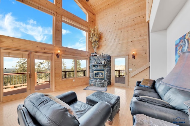 living room featuring wood walls, a stone fireplace, light wood-type flooring, and high vaulted ceiling